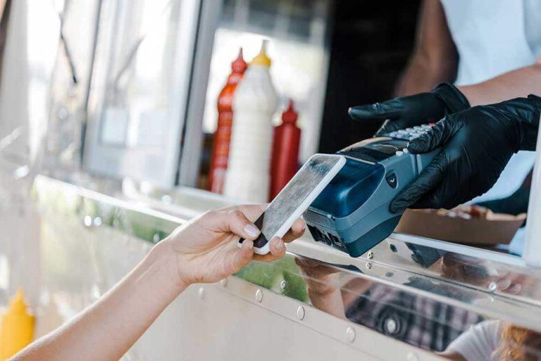 A person is using a mobile phone to pay for food at a food truck using Vendor Management Systems.
