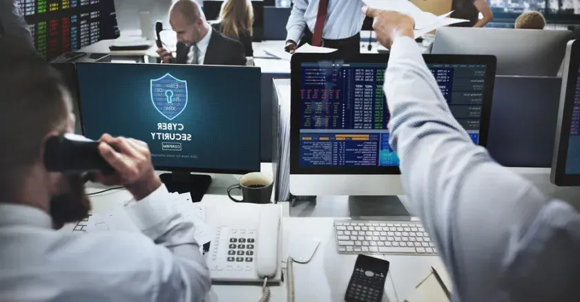 一群金融专业人士在办公室里工作，电脑屏幕上显示着网络安全标志.